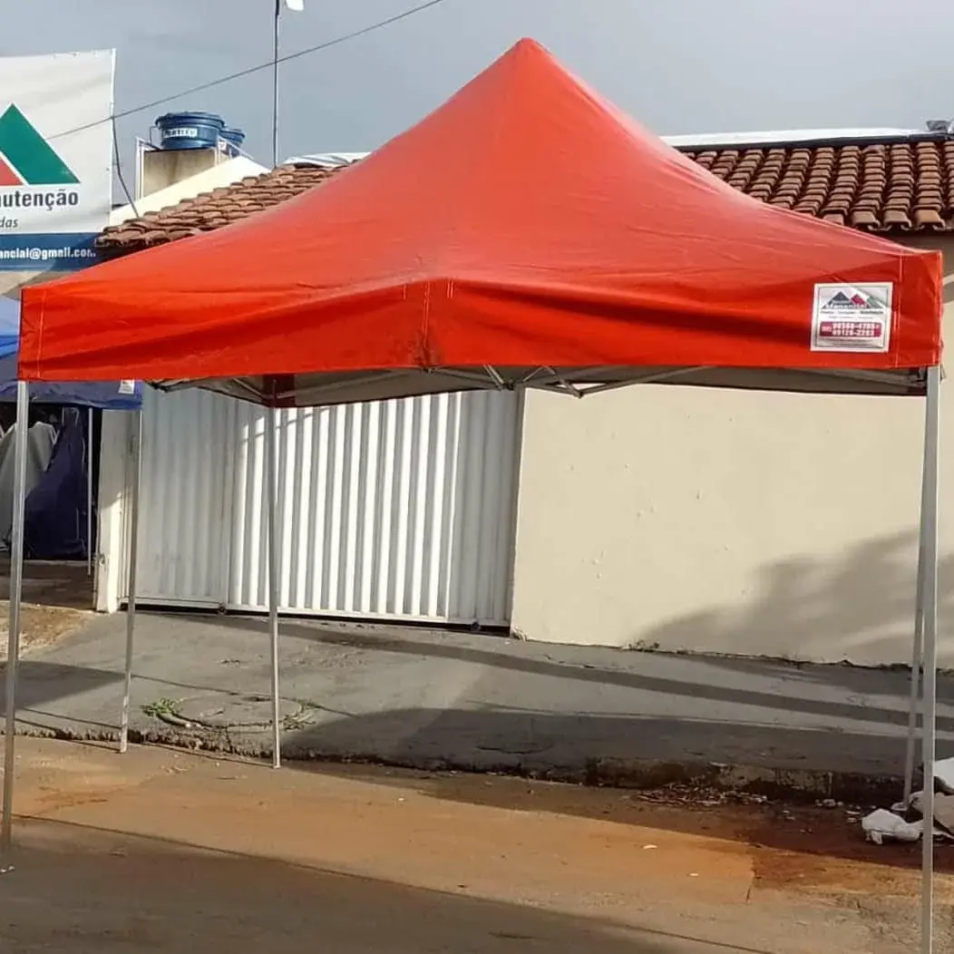 Tenda sanfonada vermelha montada com estrutura metálica clara e identificação Manancial