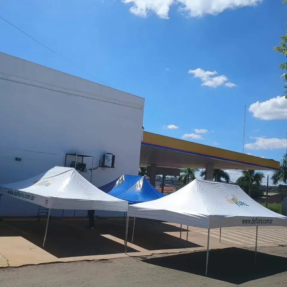 Tendas brancas personalizadas e uma tenda azul montadas em conjunto em área externa
